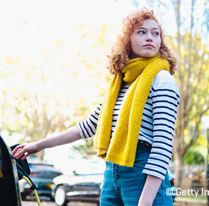 Une femme avec un foulard jaune recharge une voiture électrique
